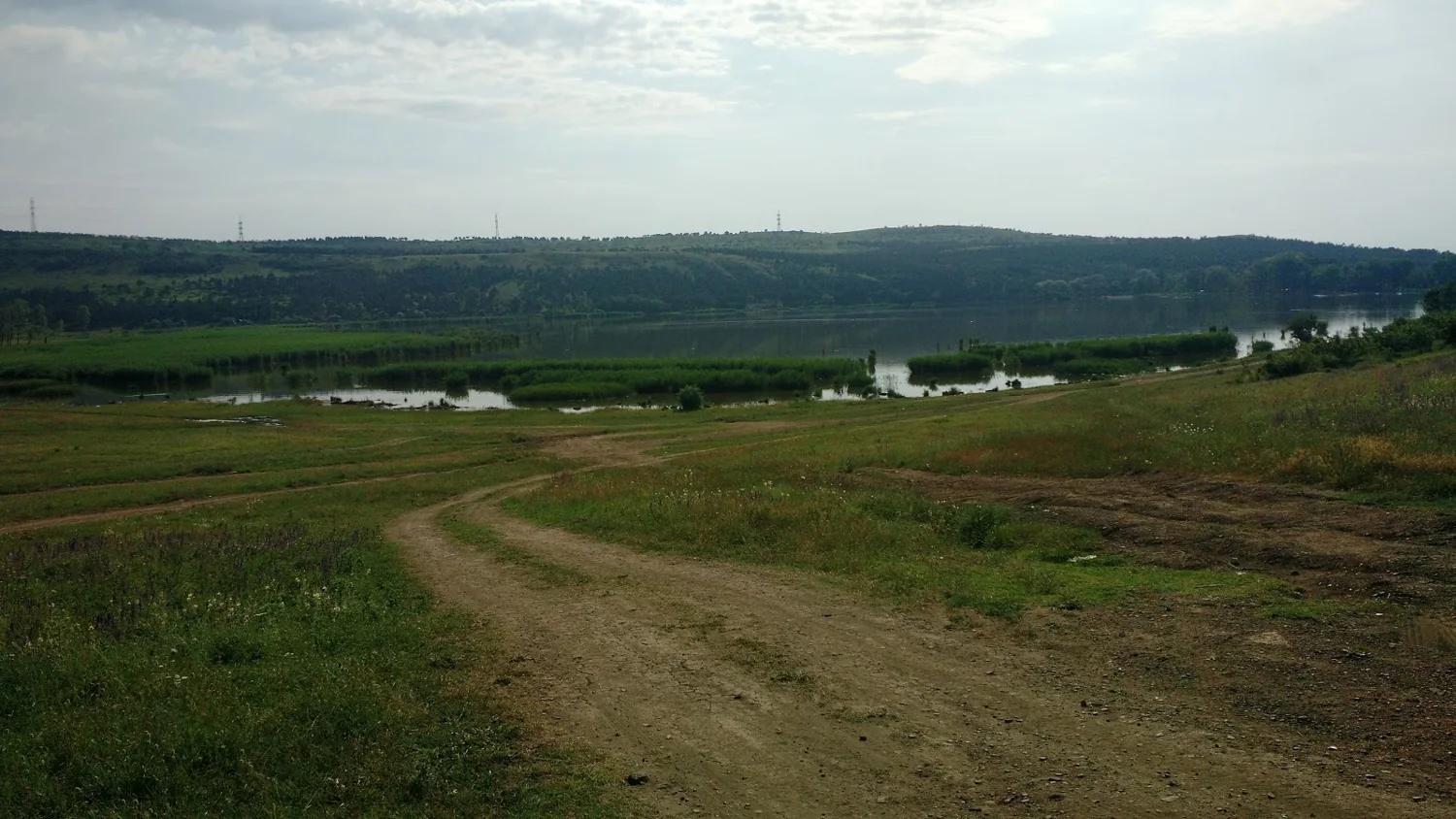 Dirt track descending through grass towards water and distant hills
