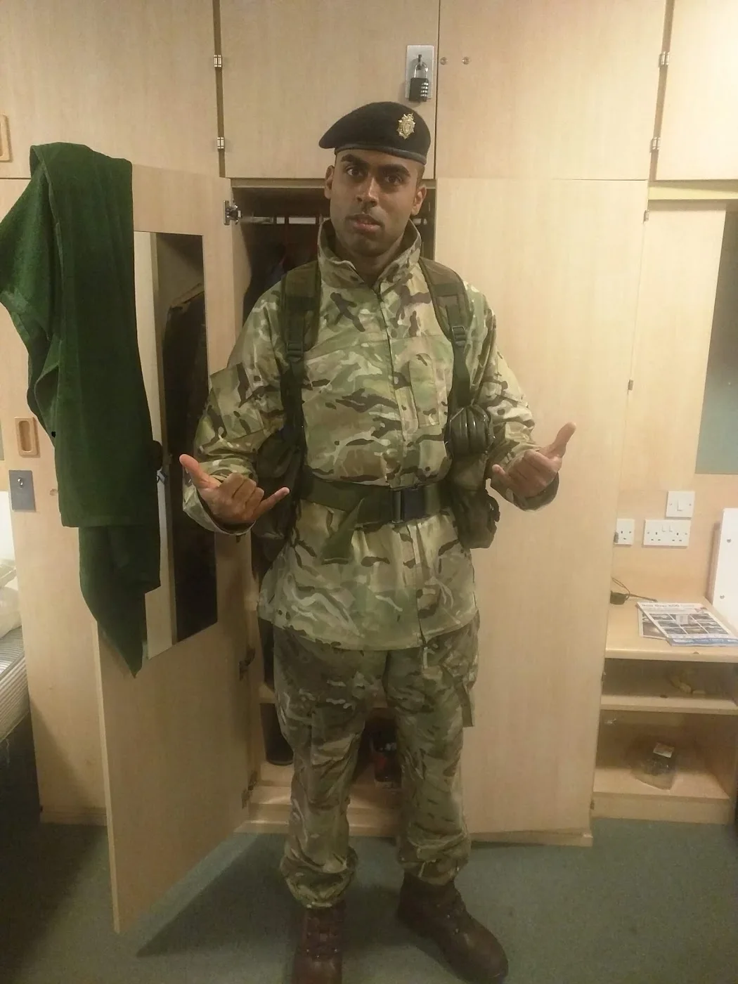 Deepak Shukla in uniform and beret, with boots and equipment, beside open storage cupboards.