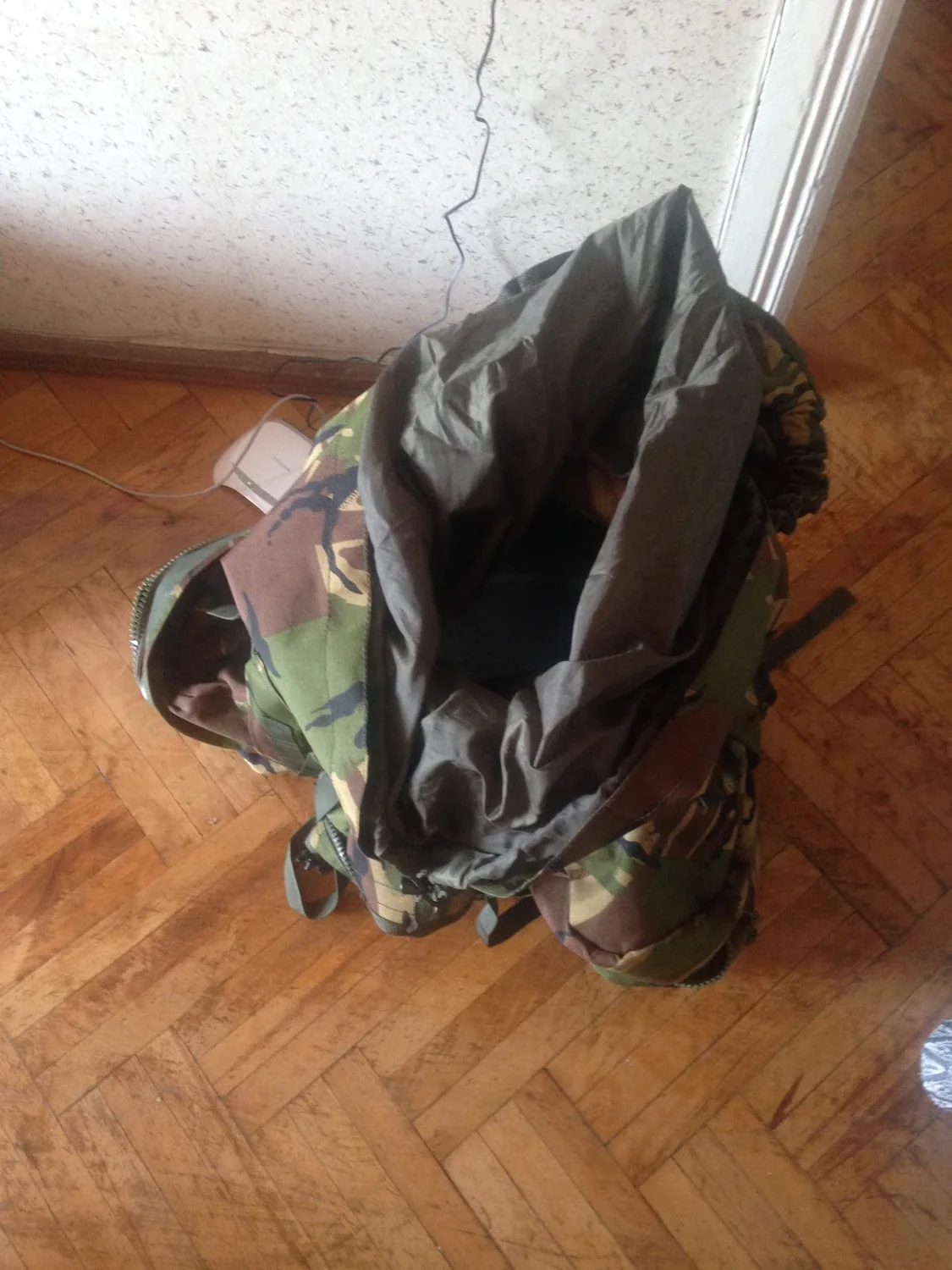 Open camouflage rucksack with dark lining on a wooden floor