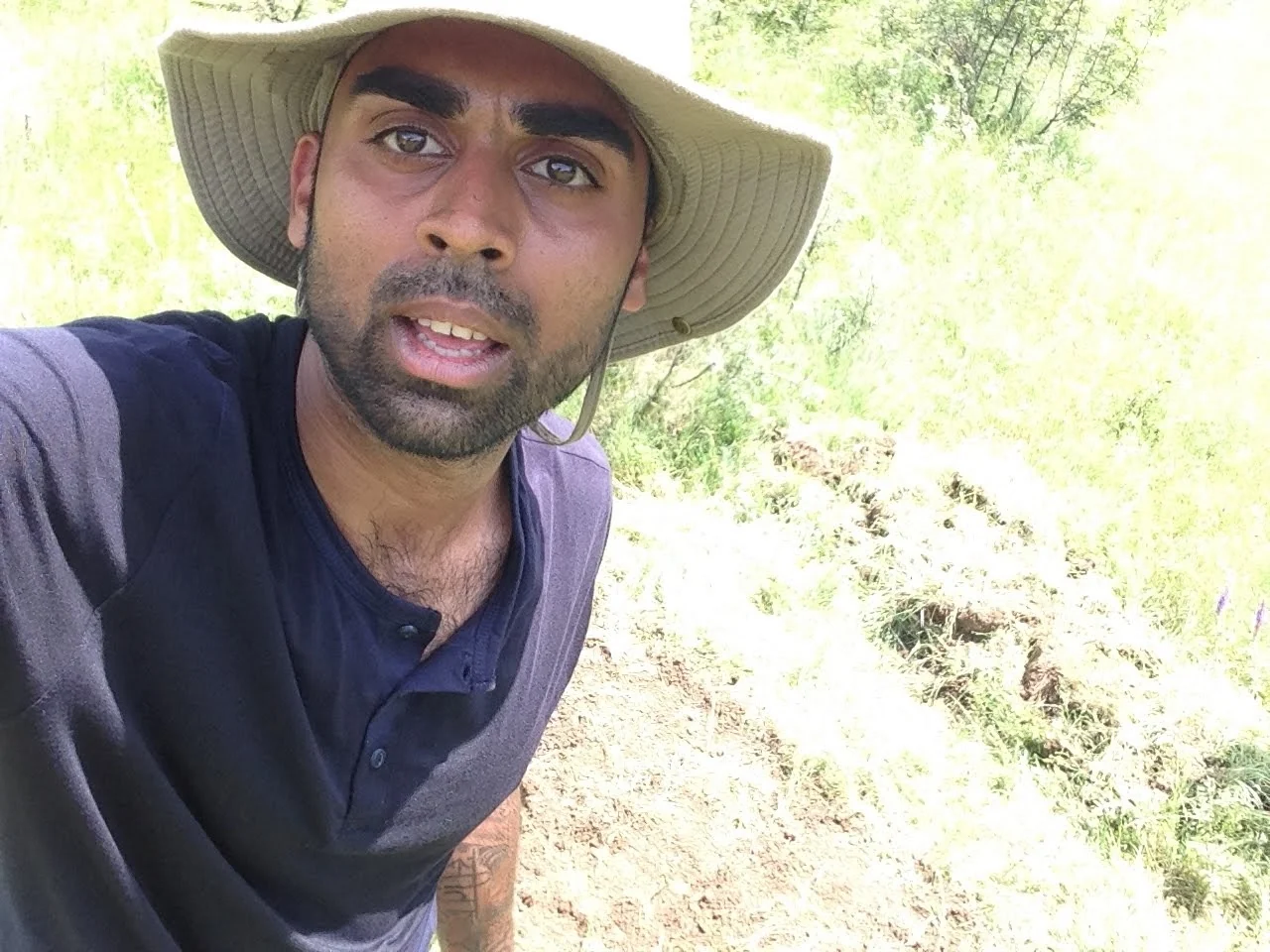 Deepak Shukla wearing a broad-brimmed hat beside a grassy hillside path
