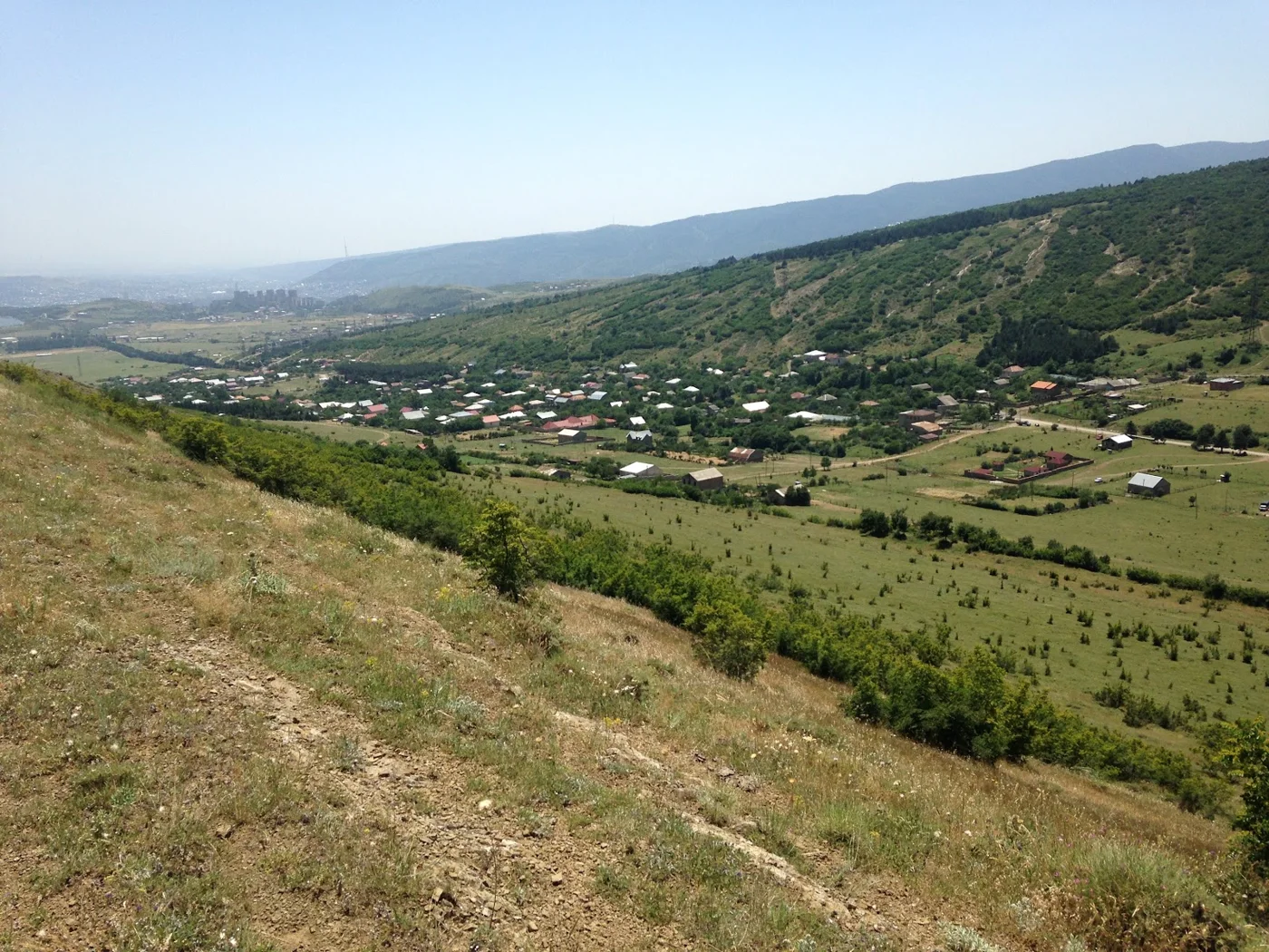 Green valley with small houses, distant hills and blue sky